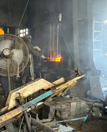 Industrial steel worker using a metal forging press to shape glowing hot molten metal in a factory.