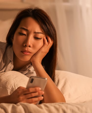 A tired woman lying in bed using a smartphone late at night, suffering from insomnia and sleep deprivation.