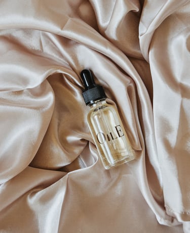 A glass facial oil dropper bottle resting on luxurious champagne silk fabric.