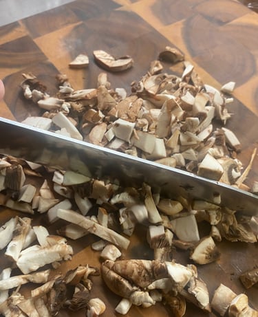 Close-up of a hand chopping fresh white button mushrooms on a wooden cutting board with a silver chef's knife, preparing