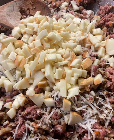 Close-up of a pan filled with ground meat and mushroom mixture, topped with shredded parmesan cheese and diced apples, ready