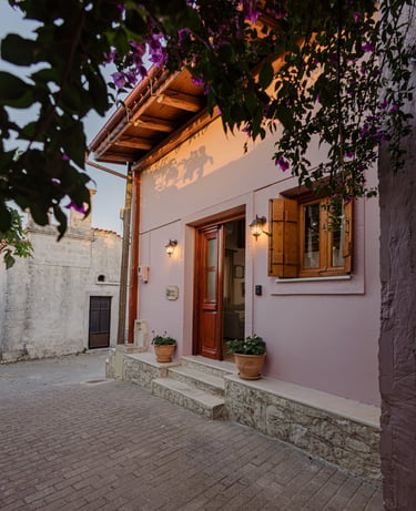 Charming cottage entrance: soft pink exterior, wooden doors, vibrant purple flowers