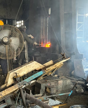 Industrial steel worker using a metal forging press to shape glowing hot molten metal in a factory.