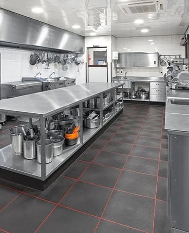 A large stainless steel table with multiple storage shelves used as a central workstation in a commercial kitchen.