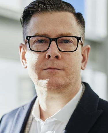 a man in a suit and glasses standing in front of a window