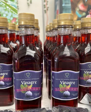 Botellas de vinagre de arándanos artesanales con tapas doradas exhibidas en filas en un mercado loca