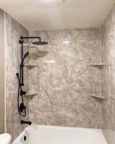Elegant bathtub and shower combo featuring marble-look wall panels, matte black rainfall showerhead, and adjustable handheld