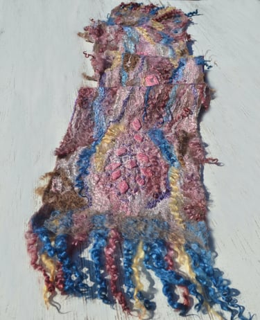 Handmade nuno felted scarf with colorful wool fibers and silk textures on a white wooden surface.