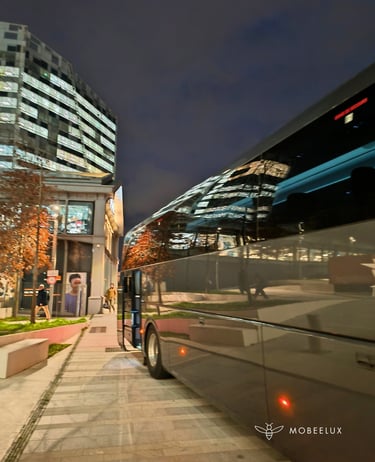 Luxury charter bus parked on a city street at night with reflections of modern office buildings.