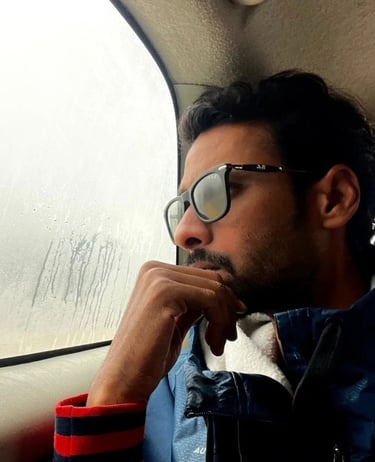 a man named Alok Dinesh in a blue jacket and sunglasses sitting in a car