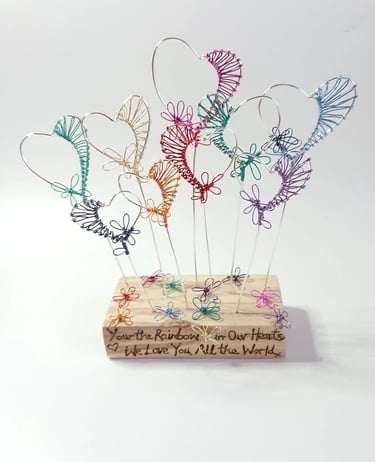 Cozams quirky hearts, seven in coloirs of the rainbow in wood reflecting flowers in garden