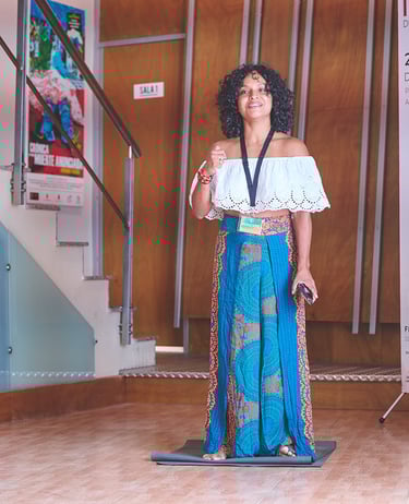 una mujer afrodescendiente con top blanco y falda larga azul hablando en un escenario