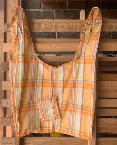 a handmade shopper bag in orange check with a small pouch attached hanging on a wooden pallet