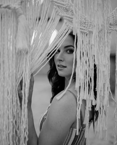 Monochromatic image of a woman partially obscured by a textured macrame textile art piece.