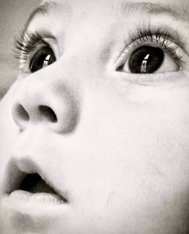 Black and white close-up of a baby girl's face, looking upward with wide eyes, capturing a sense of wonder and innocence