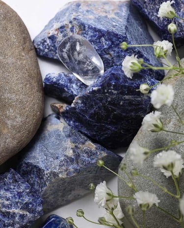 Cristales de sodalita azul en bruto y piedras de río lisas con flores blancas