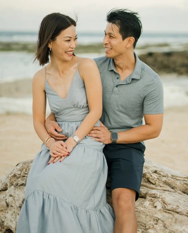 Parents sharing a relaxed moment by the shoreline during a family photography session at The Ritz-Carlton Bali.