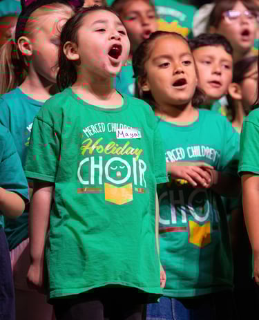 Diverse group of children in green holiday choir t-shirts singing together during a musical performance.