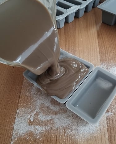 Soap mixture being poured into silicone molds on a wooden table.