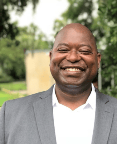 Dollar Harmony Coach Wildo in a suit and white shirt smiling