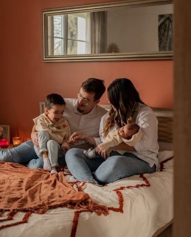 une famille de quatre personnes assis sur un lit avec un bébé dans les bras