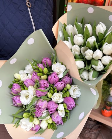 Fresh bouquets of white tulips and purple blossoms wrapped in polka dot paper for a floral gift.