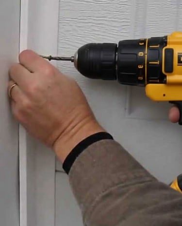 Handyman using a DeWalt cordless power drill to drive a screw into white trim for home repair.