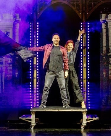 Professional magicians performing a live stage magic show with purple smoke and theatrical lighting.