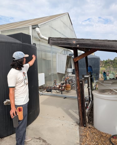 Person in baseball hat gesturing to large water tanks