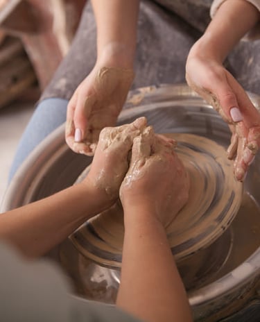 Manos dando forma a una vasija de barro en un torno de alfarería durante una clase de cerámica.
