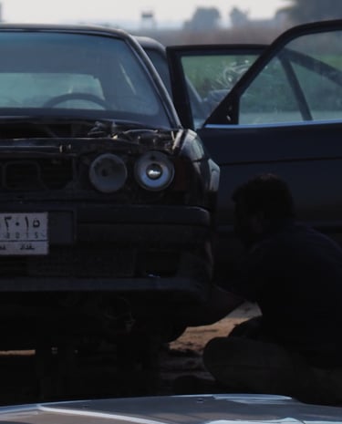 a group of Arab men in traditional clothes overlooking the dismantling of an old BMW