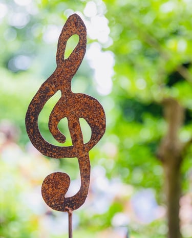 Ein metallener Notenschlüssel, im Hintergrund ein Garten.