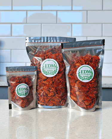 Tres tamaños de envases con tomates cherry deshidratados, sobre mesada de mármol.