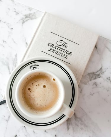 a frothy cup of coffee and a gratitude journal on a marble table