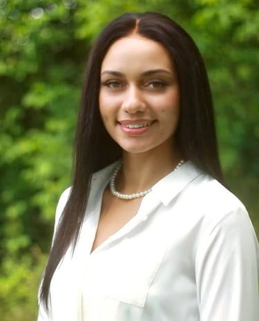 Professional portrait of a woman with long dark hair wearing a white blouse and pearl necklace outdoors.