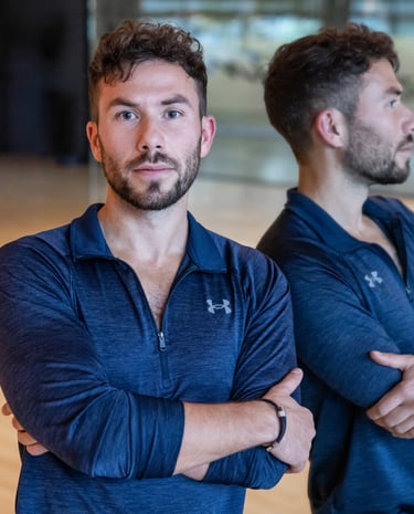Professional male fitness trainer in blue athletic wear posing in a gym studio with mirror reflection.