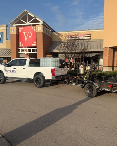 White commercial pressure washing truck and trailer parked at a retail shopping center.