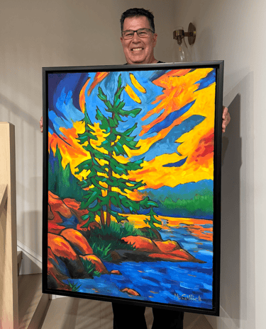 Mitch Gillick holding a painting of a Muskoka sunset