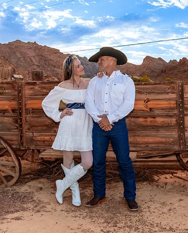 a man and woman in cowboy attire standing in front of a wagon