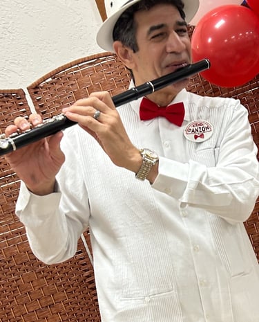 Maestro Bobby Ramirez in a white suit and red bow tie playing flute