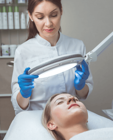 Dermatologist examining a patient’s facial skin using a magnifying light during a skin evaluation.