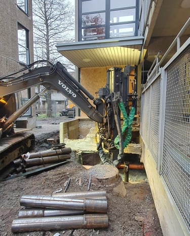 A Volvo excavator with a hydraulic pile driver attachment installs steel foundations at a construction site.