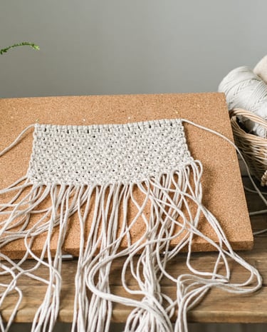 tapiz de macramé hecho a mano sobre un tablero de materiales de trabajo artesanal.