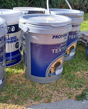 Prominent Paints exterior textured paint buckets and a step ladder on a lawn for a home painting project.