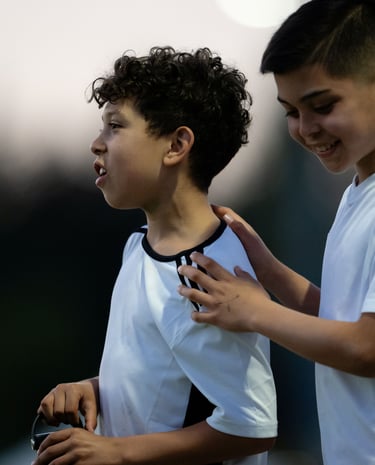 One boy watching an unseen soccer ball go wide and a second boy patting him on the back.