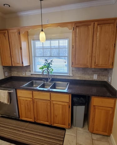 Modern kitchen with oak wood cabinets, dark granite countertops, and a triple-basin stainless steel sink.