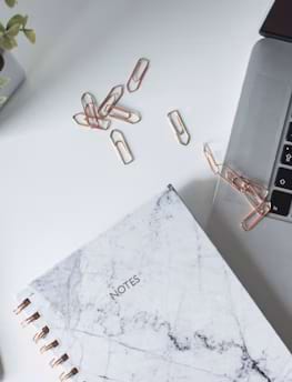Marble notebook labeled notes with paper clips and laptop on white desk, representing skincare blog