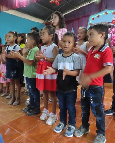 A group of children stand together clapping and singing.