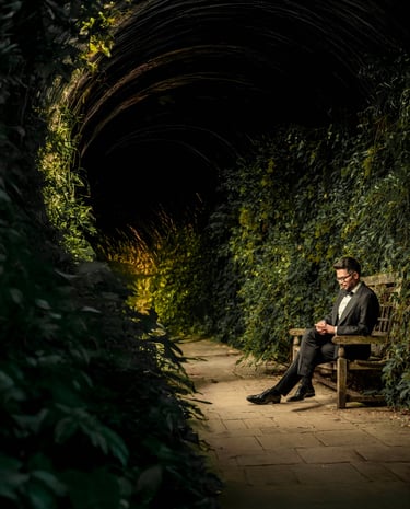 Groom sitting on a wooden bench in a vine-covered tunnel, captured by Fred Art Studio.