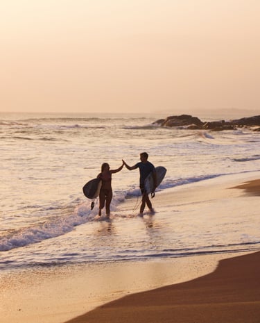 two surfers high five by the ocean